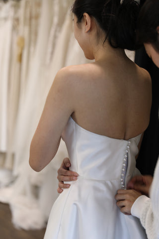 woman buttoning brides wedding dress up