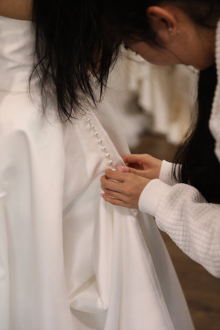 woman buttoning up a brides dress