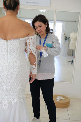 woman sewing sleeve on another womans wedding dress