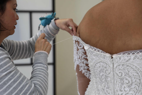 woman sewing sleeve on brides wedding dress