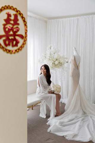woman wearing robe seated on sofa in front of her wedding dress