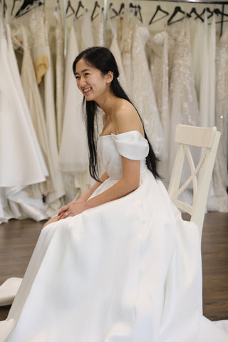 woman wearing wedding dress sitting in chair in front of racks of gowns