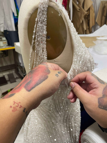 woman with red tattoos hand sewing lace wedding dress