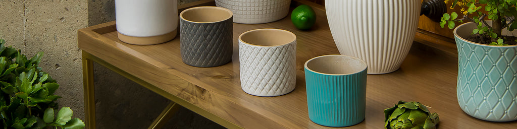 jarrones de cerámica de diferentes texturas y colores sobre mesa de madera en un entorno natural