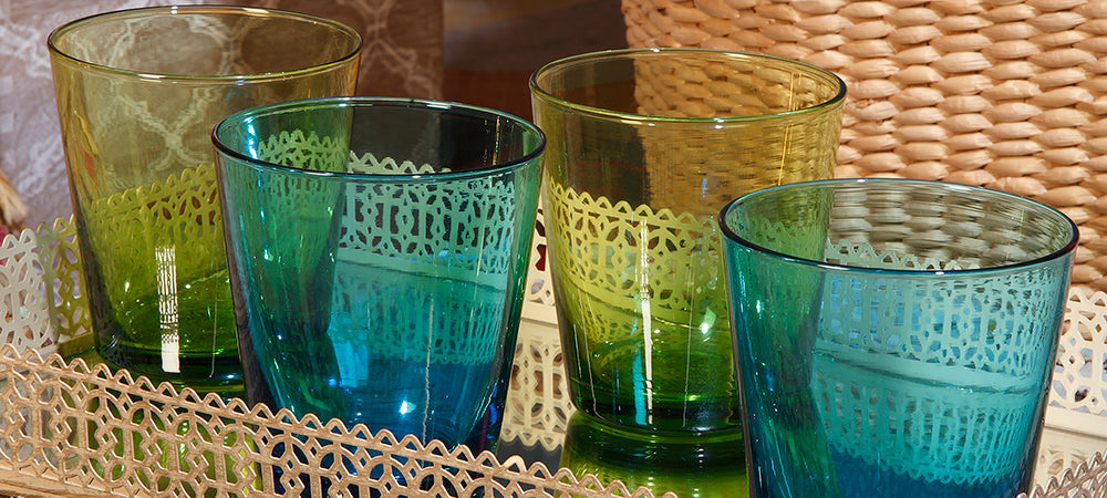 primer plano de cuatro vasos de cristal azules y verdes sobre una charola dorada