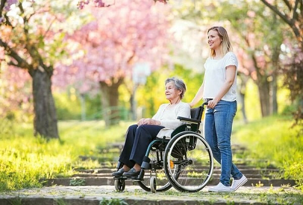 older woman being pushed around by caregiver in a garden