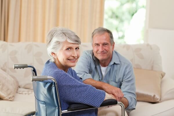 smiling woman in a wheelchair with man on a couch 