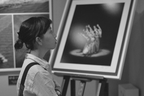 A grayscale photo of a woman standing near painting