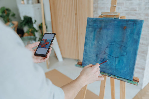 A person painting on a canvas while holding a smartphone