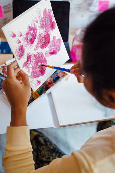 A photo of a girl drawing pink petaled flowers on a white paper