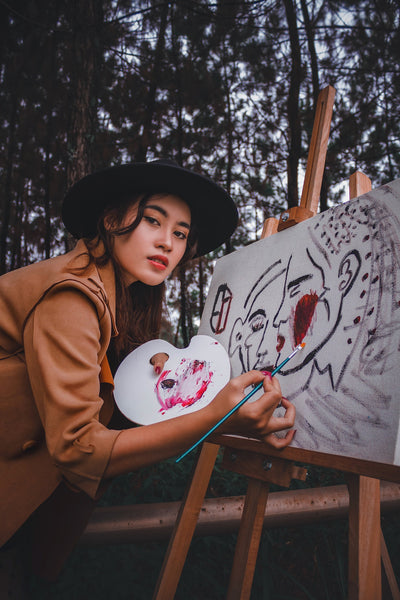 A photo of woman holding paint brush close to a painting