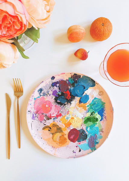 paint palette with paints on a ceramic plate close to a fork and a knife