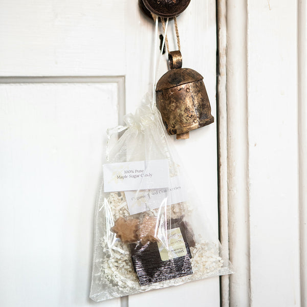 White organza bag hanging from a doorknob that contains a box of Tangle Chocolate slivers, maple sugar candy, dried cranberries