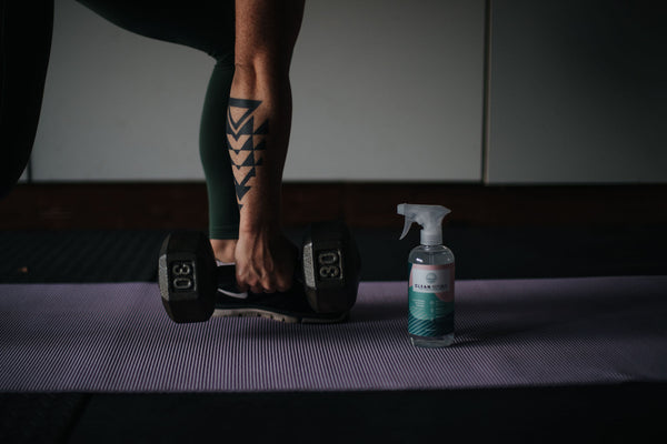 woman lifting a dumbbell and a spray bottle of cleaning solution