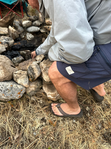 man in flip flops and shorts lighting a campfire