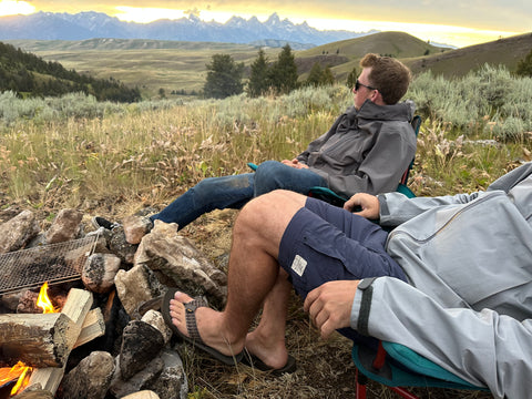 two men sitting by a campfire on a mountain at sunset