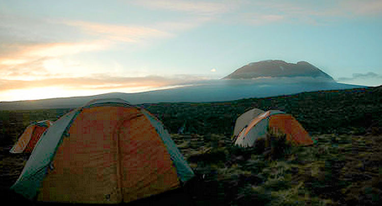 a group of tents on the mountain with a sunrise in the background