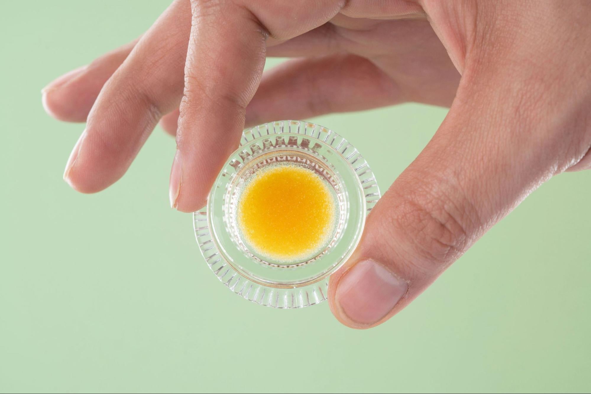 Hand holding small glass full of cannabis extract