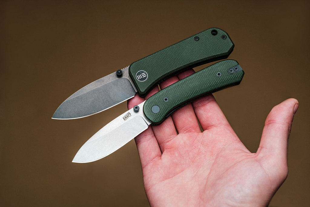 hand holding two knives we banter and knafs lander with green micarta