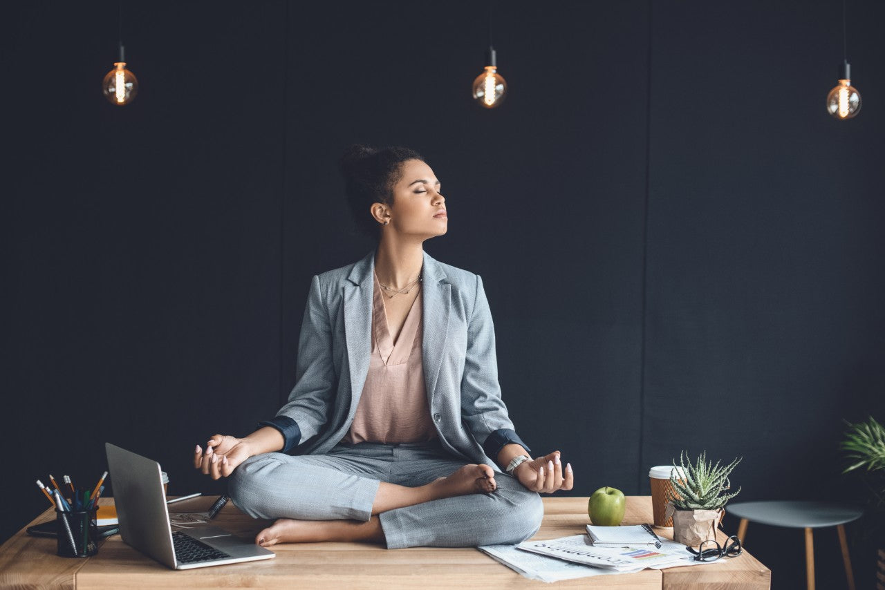 Female office worker sitting on her desk meditating - Meditation 101 | Eco Yoga Store