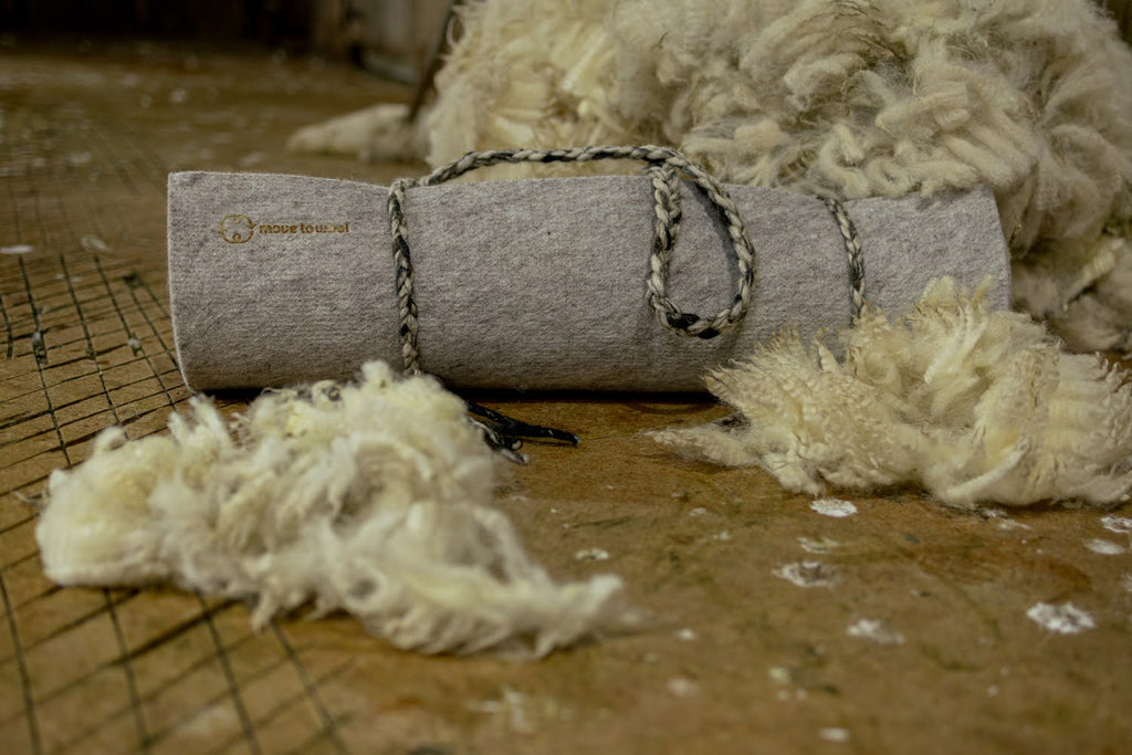 Move to Wool Movement Mat rolled up sitting on a shearing shed floor surrounded by fleece | Eco Yoga Store