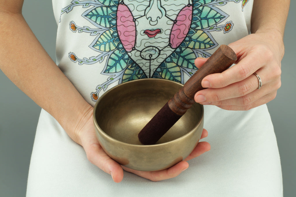 Image of hands holding tibetan singing bowl and striker poised to create sound therapy | Eco Yoga Store