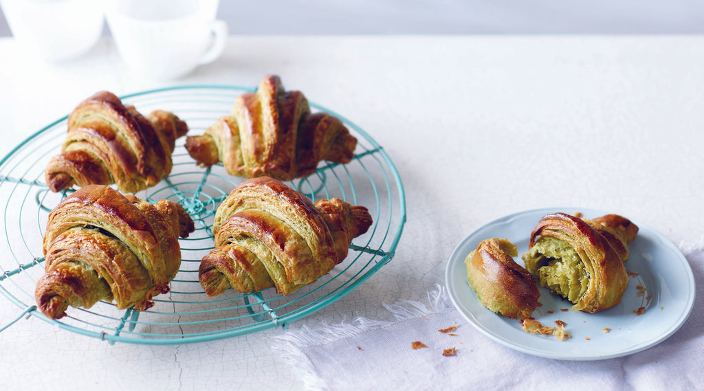 A plate of delicious matcha croissants, golden and flaky, on a wire cooling rack and plate.