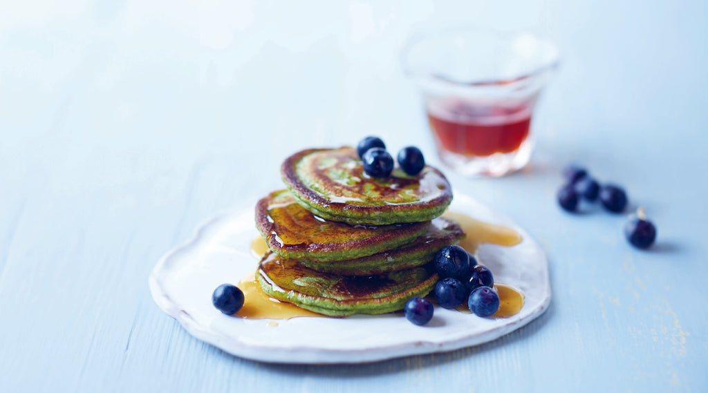 Fluffy matcha pancakes topped with juicy blue blueberries and syrup.