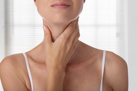 a woman touching her thyroid, she takes zinc for thyroid health