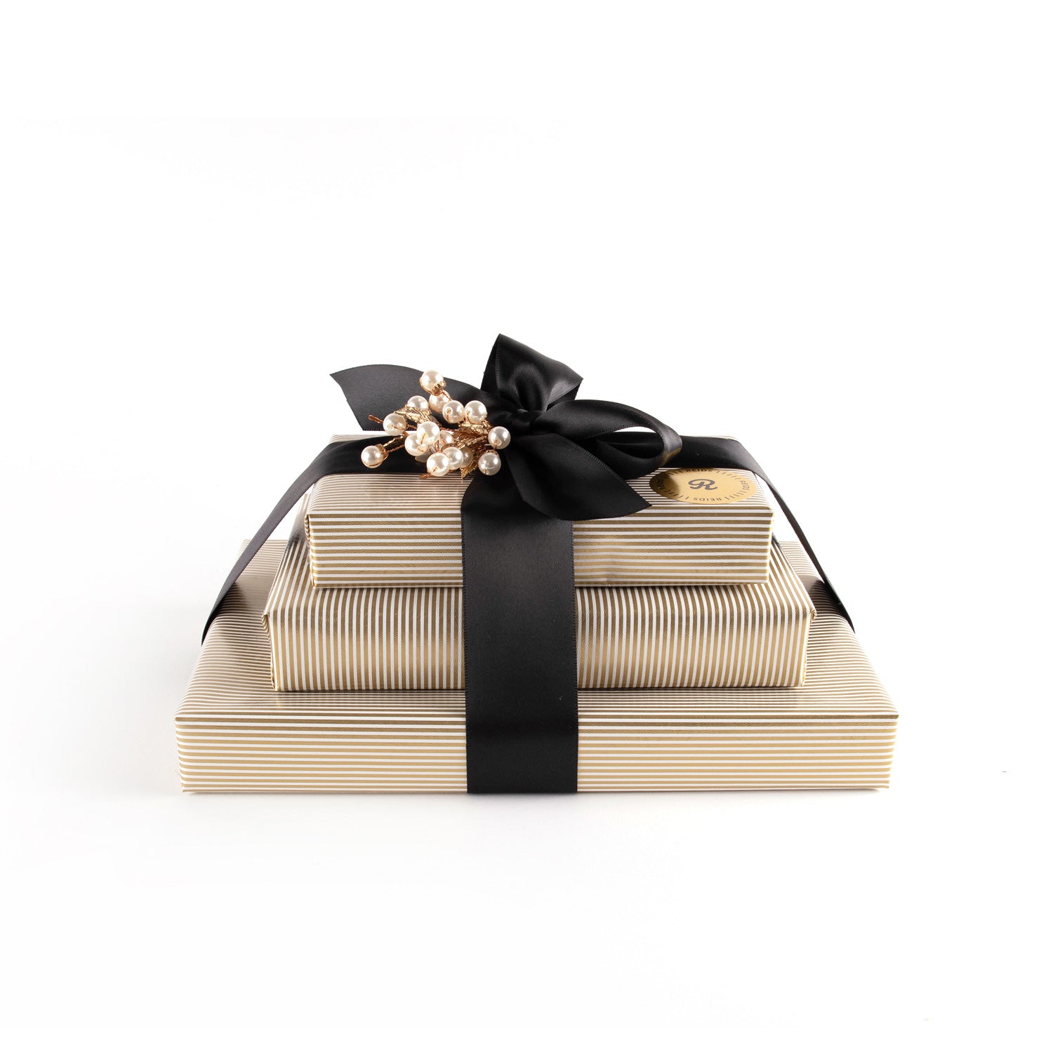 Three stacked Trio Box . Gold, and white pin-stripped wrapping paper. Tied with a black satin ribbon and white decorative piece.