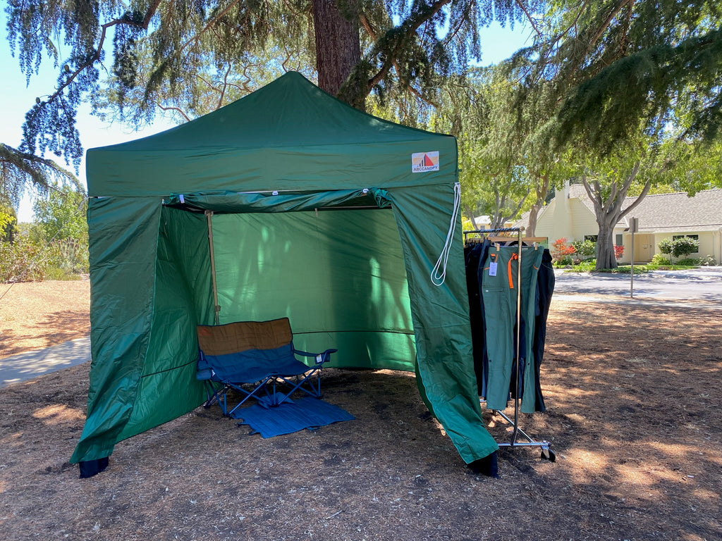 A three-sided green tent that is used for fit testing. On its right is a clothing rack with products. 