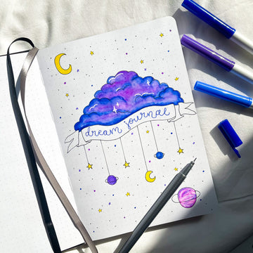 An open journal on a pillow with a cloud drawing and 'dream journal' title