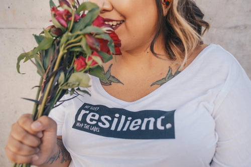 A woman smelling flowers, wearing a t-shirt that reads 'My size? resilient.' to promote body positivity and self-love