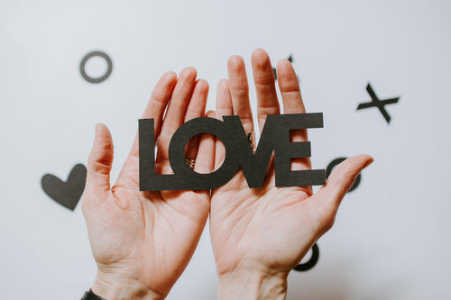 Hands holding black cutout letters spelling the word LOVE