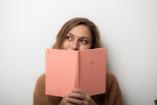 Woman holding an open pink journal and peering over the top