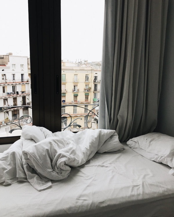 An unmade bed in front of a balcony window