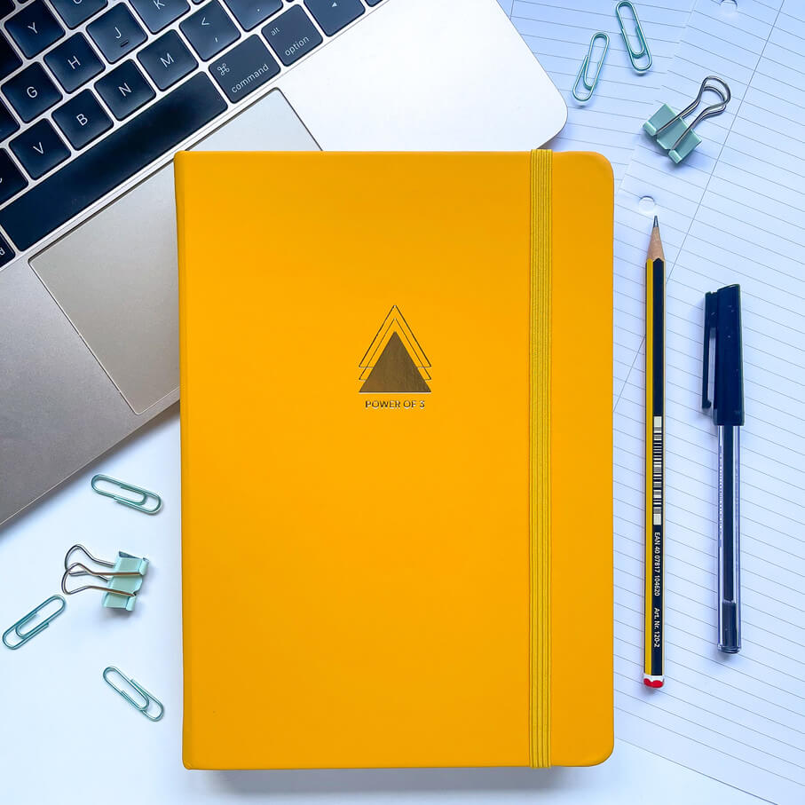 yellow journal on a desk surrounded by stationery