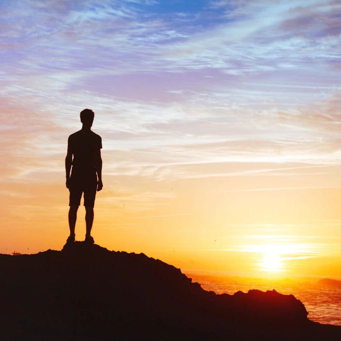 The silhouette of a person standing on the top of a mountain looking at the sunset