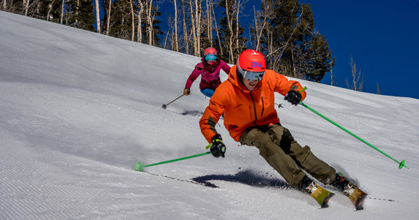 Skiers carve on a steep groomed run.