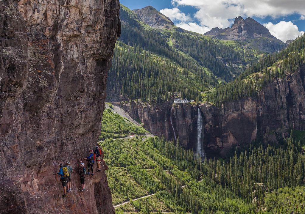 Climbers are suspended on a cliff on Telluride's Via Ferrata with Bridal Veil Falls in the background.