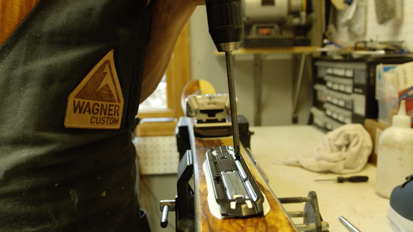 A person mounts a ski binding to a ski.