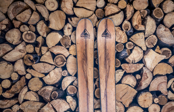 A pair of Wagner Custom wood veneer skis sit in front of a wood pile