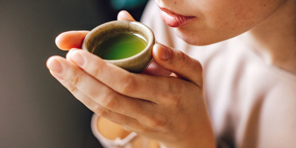 Woman drinking green tea from a small ceramic cup.