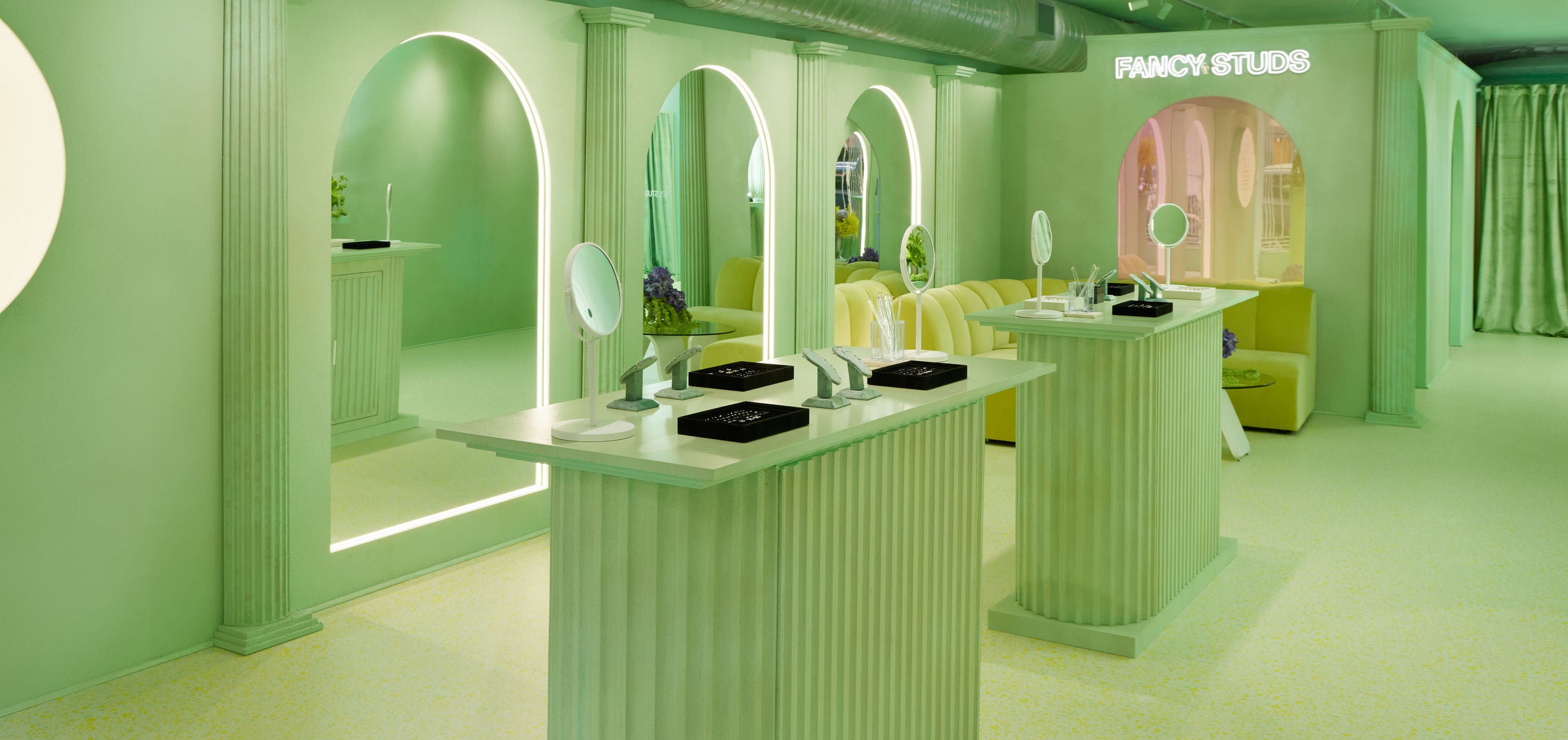 Interior of a stylish green-toned piercing studio with product display counters and decorative arches.