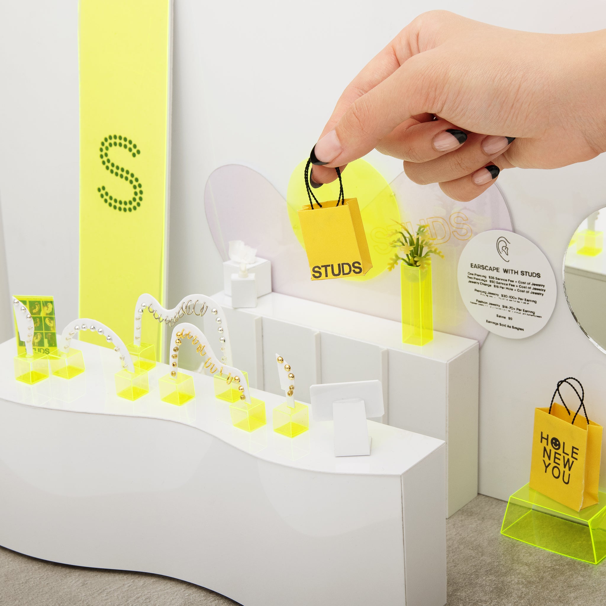 Studs branded transparent yellow pouch on a flat surface with stickers, earrings and dime bags.