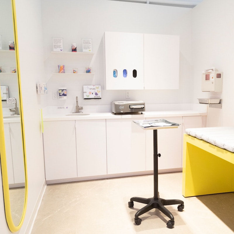 An image of the inside of a piercing room with a tray and bench with a mirror on the wall.