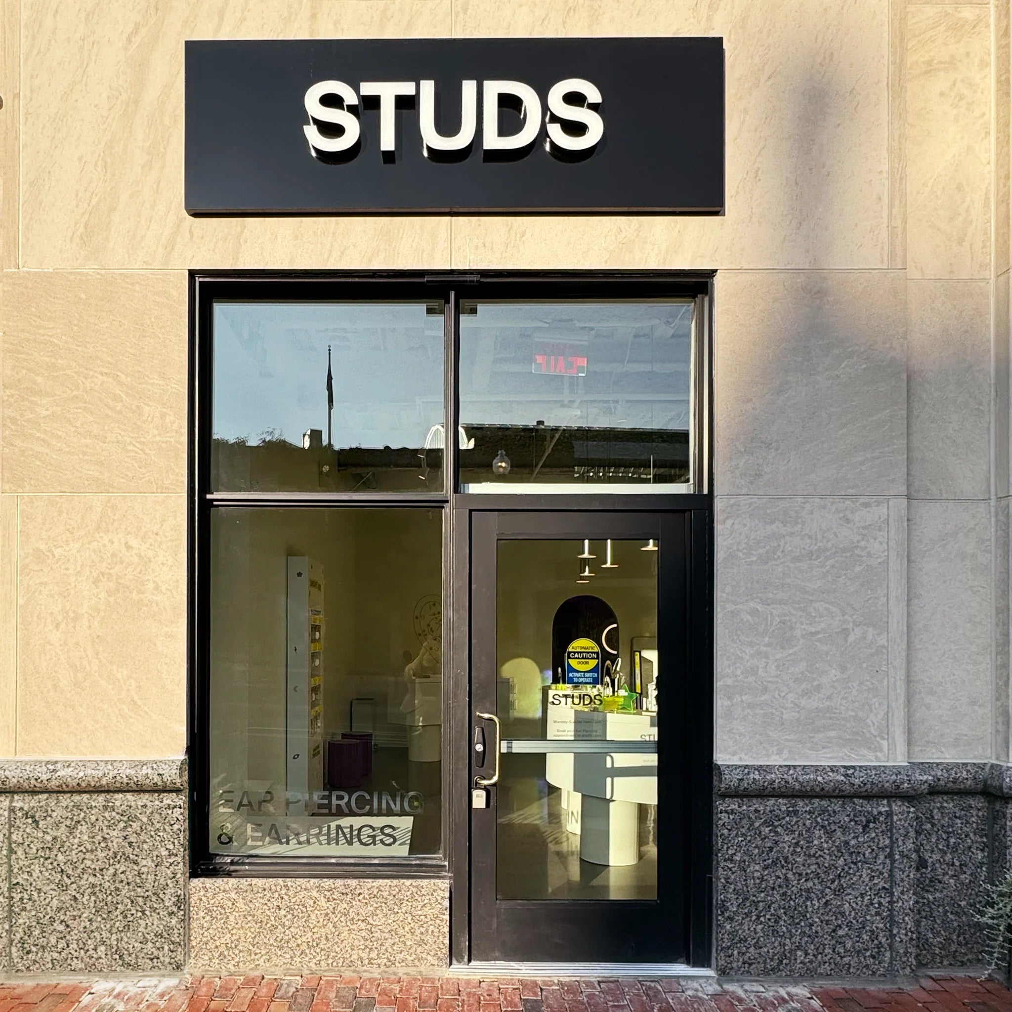 Storefront of a shop named 'STUDS' offering ear piercing and earrings.
