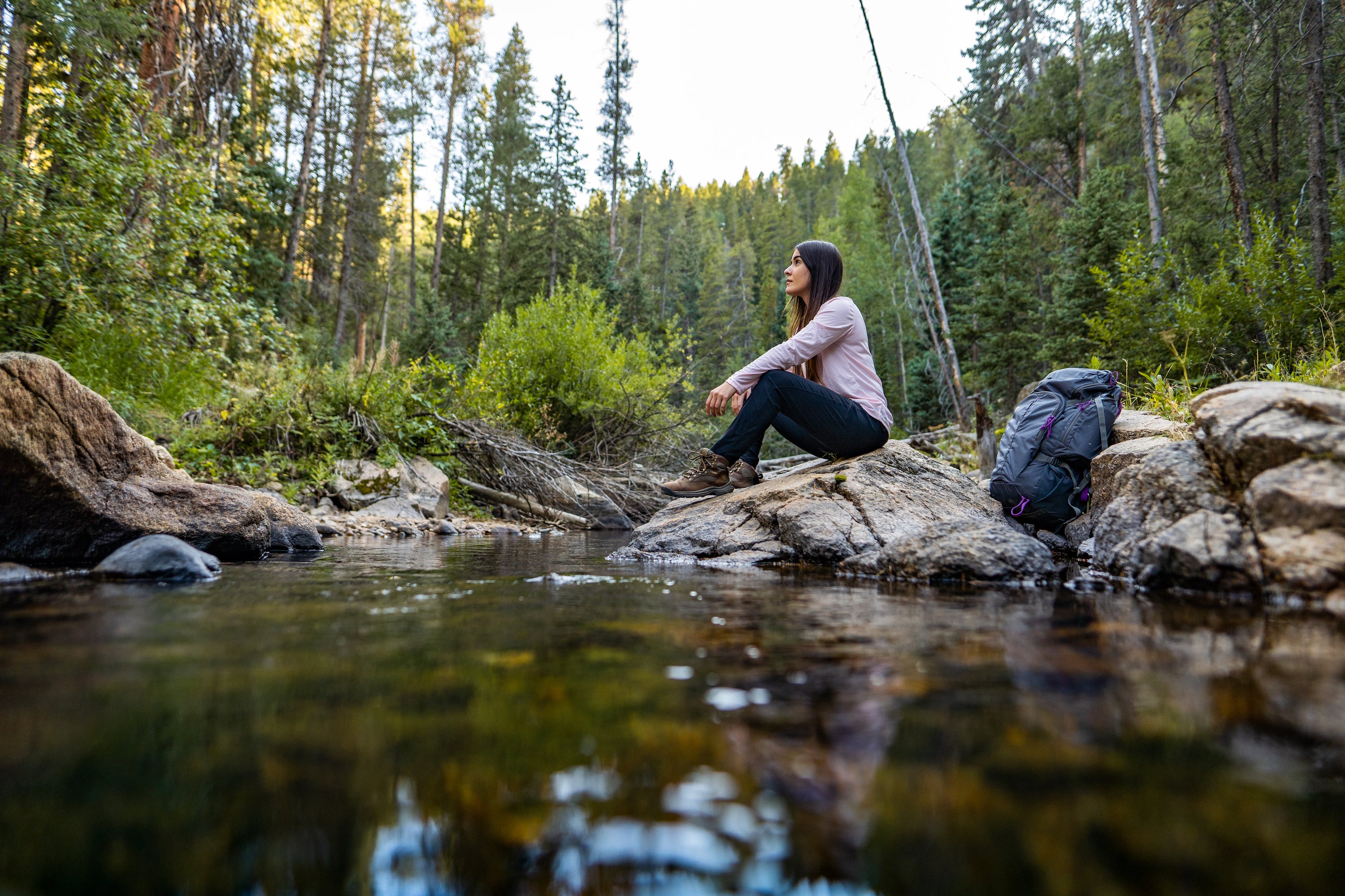 Woman hiker wearing base layer sitting by stream