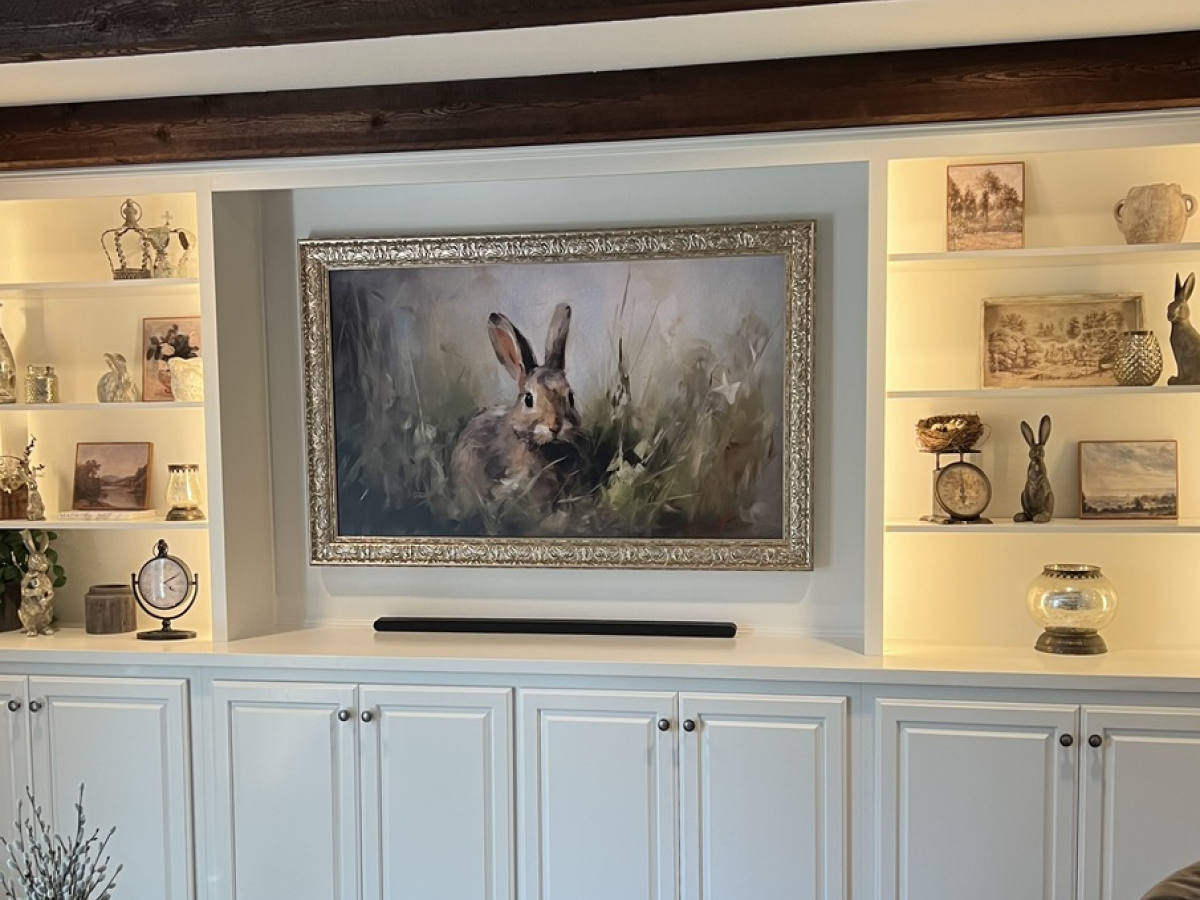 Painting of a rabbit on a wall above white cabinets, flanked by shelves with decorative items.