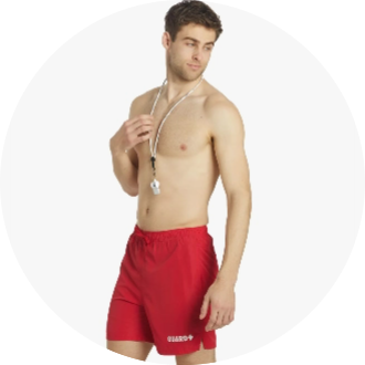 A male lifeguard model is wearing red swim trunks with a "GUARD+" logo and a whistle around his neck. The swim trunks are designed for lifeguard duties, providing comfort and visibility.